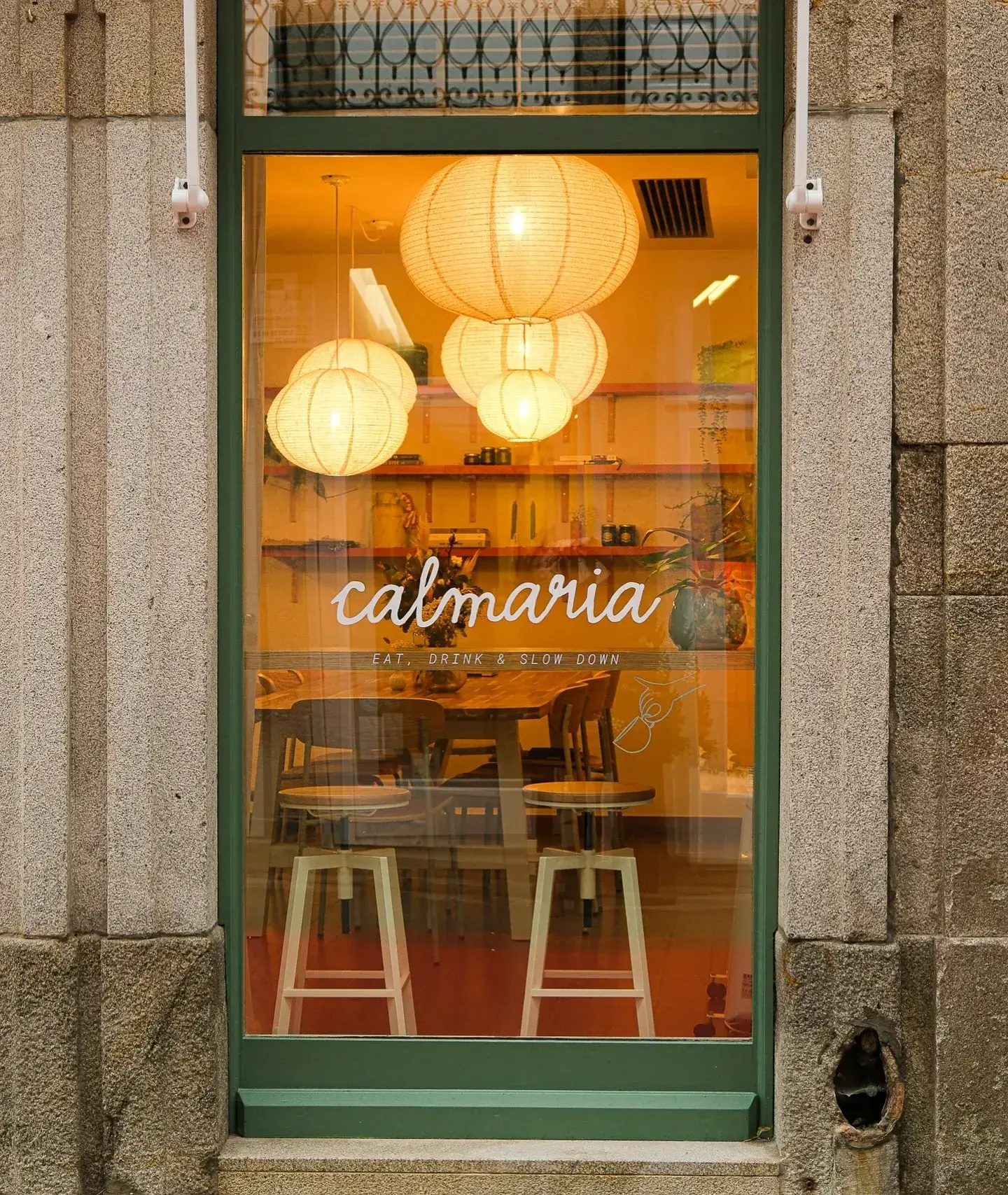 Uma janela de restaurante acolhedora com três lanternas penduradas e o nome calmaria.