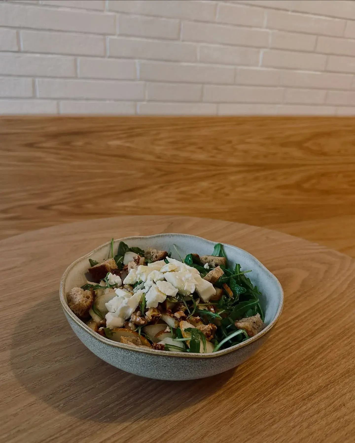 Uma salada fresca com verduras, maçãs fatiadas, nozes, croutons e queijo feta esfarelado, servida em uma tigela rústica.