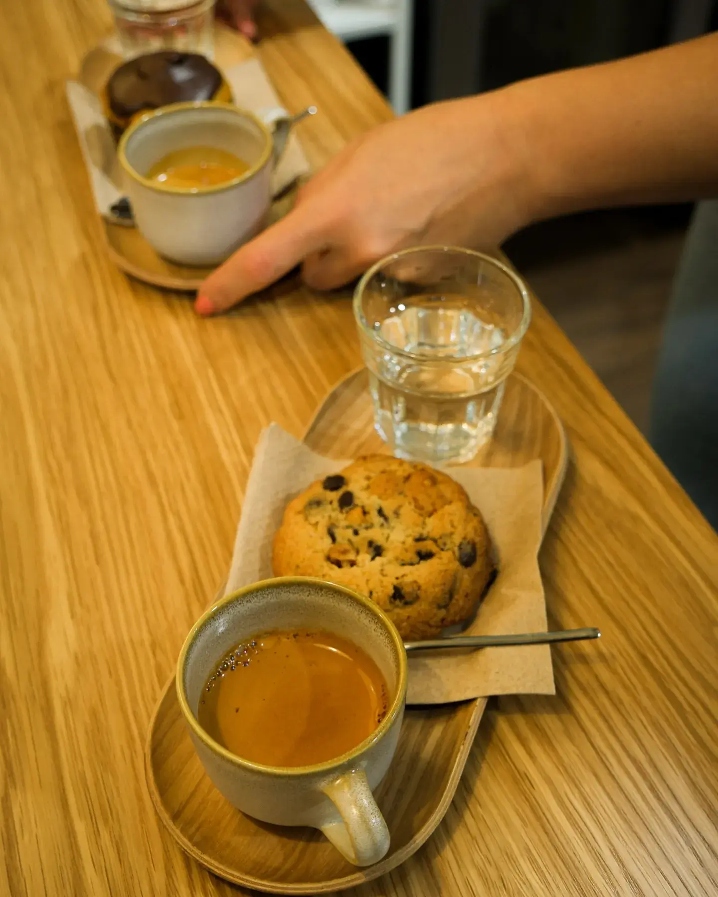 Uma chavena de espresso, um biscoito e um copo de água sobre uma tábua de madeira.
